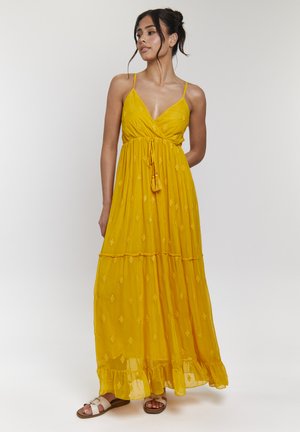 Robe maxi jaune avec bretelles spaghetti réglables, décolleté en V, ourlet volanté à plusieurs niveaux et motifs en diamant subtils. S'associe avec des sandales blanches.