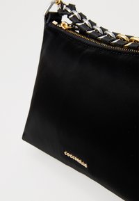 Borsa nera con zip dorata, tracolla a catena intrecciata con pelle nera e un piccolo logo dorato del marchio sulla parte anteriore inferiore.