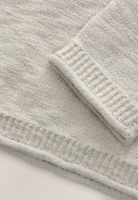Maglione grigio chiaro lavorato a maglia con polsini e orlo a costine. Tessuto morbido e testurizzato con lievi variazioni di spessore del filo. Vista ravvicinata.