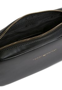 Μαύρο δερμάτινο πορτοφόλι Tommy Hilfiger με χρυστό φερμουάρ μισάνοιχτο, που δείχνει την εσωτερική επένδυση με λογότυπο.