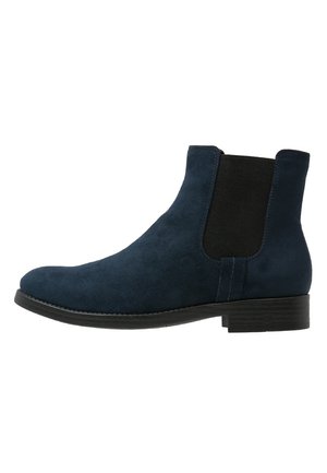 Bottines en suede marine à panneaux latéraux élastiques, bout rond et semelle plate en caoutchouc. Texture lisse avec un design minimaliste sans quincaillerie visible.