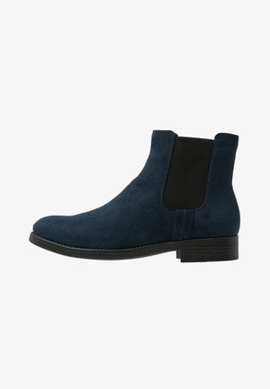 Bottines en suede marine à panneaux latéraux élastiques, bout rond et semelle plate en caoutchouc. Texture lisse avec un design minimaliste sans quincaillerie visible.