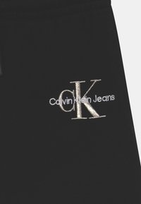 Detailní záběr na černou látku s bílou vyšitou logem "Calvin Klein Jeans" se velkými iniciálami "cK".