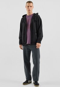 Czarna bluza z kapturem zapinana na zamek z troczkami, na fioletowej koszulce i szarych dżinsach. Strój uzupełniają czarno-białe trampki.