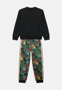 Μαύρη φούτερ μπλούζα με στρογγυλή λαιμόκοψη και μακριά μανίκια, σε συνδυασμό με φλοράλ φόρμα με πράσινα, κίτρινα και κόκκινα λουλούδια και ρίγες ως διακοσμητικά στοιχεία.