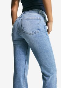 Lyseblå denim jeans med en tætsiddende pasform, der har to baglommer og lige ben. Glat tekstur med subtile sømdetaljer.