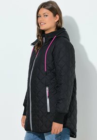 Giacca trapuntata nera con cappuccio. Presenta coulisse rosa, una cerniera frontale completa e tasche laterali con cerniera con dettagli di colore a contrasto.