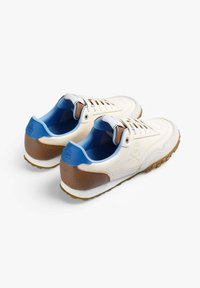 Baskets blanches avec un talon texturé marron, des accents bleus sur la languette et la doublure, et une semelle en caoutchouc avec de petits motifs de traction.