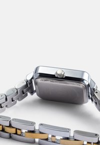 Reloj de metal plateado con caja rectangular, corona redonda y pulsera de metal bicolor con acentos en oro y plata.