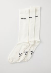 Tres pares de calcetines blancos de punto hasta la rodilla, con el texto negro "CPNHGN" en los laterales y un logo en la parte inferior.