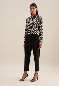Camicia a righe zebrate in bianco e nero con colletto, abbinata a pantaloni neri su misura e tacchi alti neri con cinturini. Texture del tessuto liscia.