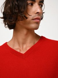 Maglione rosso a scollo a V lavorato a maglia, caratterizzato da una texture morbida, un colletto a coste e una silhouette aderente. La vista ravvicinata mette in risalto i dettagli della lavorazione.