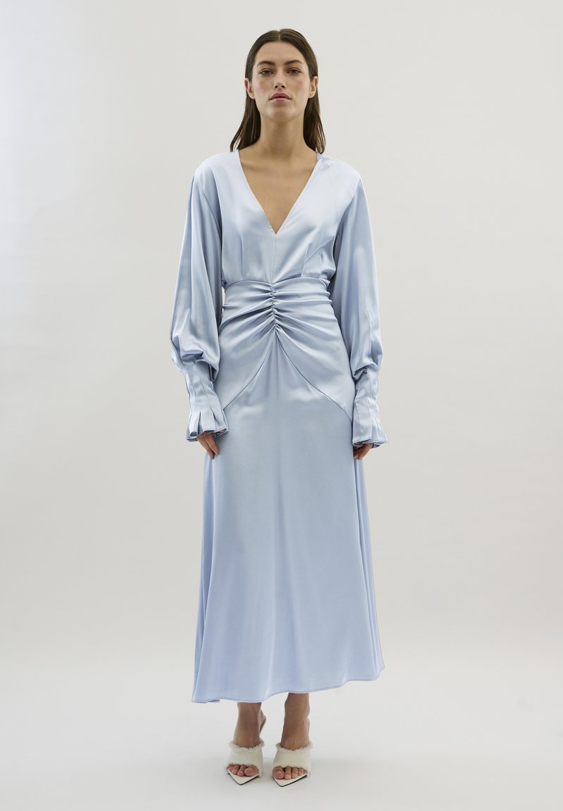 Rochie din satin bleu deschis, cu decolteu în V adânc, mâneci lungi bufredate, talie plisată și fustă netedă, fluidă. Design simplu și elegant.