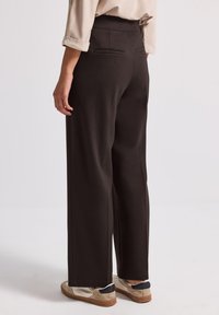 Pantalons larges marron �à taille haute, dotés de deux poches arrière et de détails de couture discrets, associés à des baskets de couleur claire.
