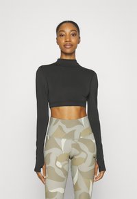 Top negro de manga larga y corte corto hecho de una tela suave, combinado con leggings de cintura alta que presentan un patrón abstracto en beige y verde.