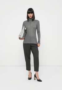 Pull noir à col roulé associé à un pantalon tailleur gris foncé, tenant une pochette en simili cuir serpent métallique et portant des talons noirs.