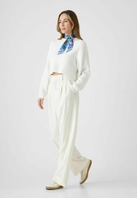 Witte cropped sweater met lange mouwen, geplooide witte broek en beige sneakers. Accessorized met een kleurrijke, patroon gescheurde sjaal.