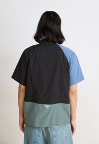 Short-sleeve shirt featuring a color-block design in black, blue, and green materials. Textured fabric with a relaxed fit and back detail.