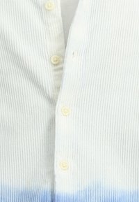 Witte geribde shirt met een verlopen blauwe zoom, bevat zes crème kleurige knopen en heeft een zachte textuur.