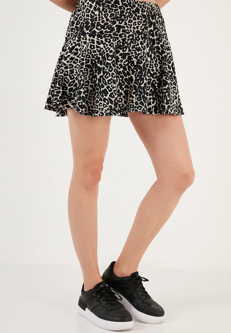 Gonna leopard print nera e beige con design svasato, abbinata a sneakers nere con suole e lacci bianchi.