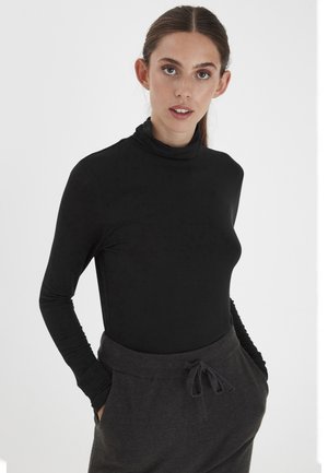 Schwarzes langärmliges Turtleneck-Shirt mit glatter Textur, kombiniert mit dunkelgrauen Jogginghosen mit Kordelzug und seitlichen Taschen in lockerer Passform.