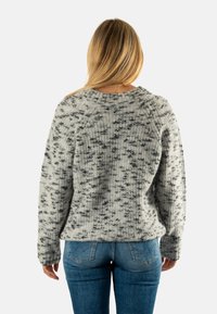 Suéter gris de punto con un patrón moteado, escote de canalé y mangas largas, combinado con jeans de mezclilla azul.
