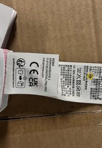 Biała metka materiałowa z czerwonymi akcentami, zawierająca instrukcje dotyczące pielęgnacji, szczegóły producenta oraz loga, w tym CE i UKCA.