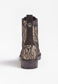 Bottine noire en dentelle avec un panneau en daim et une semelle en caoutchouc. Présente un accent de logo métallique circulaire et un motif texturé en dentelle.