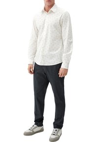 Weißes Hemd mit kleinen grauen geometrischen Mustern, langen Ärmeln und klassischem Kragen; kombiniert mit dunklen Hosen und Sneakers.