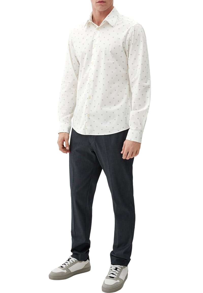 Weißes Hemd mit kleinen grauen geometrischen Mustern, langen Ärmeln und klassischem Kragen; kombiniert mit dunklen Hosen und Sneakers.