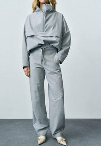 Grijze, oversized half-rits jas met lange mouwen, gecombineerd met bijpassende wijde broek en puntige, crèmekleurige schoenen. Effen stofstructuur.