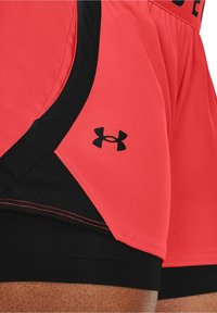Pantalones cortos deportivos rojos con acentos negros, que presentan un panel de malla y un pequeño logotipo negro. Tela texturizada con detalles de costura en contraste.