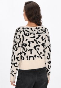 Pulover tricotat cu un fundal bej și imprimeu leopard abstract negru. Dispune de mansete și tiv cu borduri, mâneci lungi și o croială lejeră.
