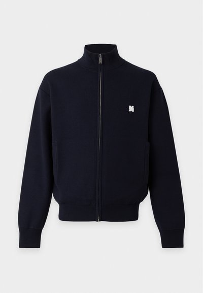 Veste noire zippée intégrale avec col montant, manches longues, poches latérales, poignets et bas côtelés, et un petit logo blanc brodé sur la poitrine.