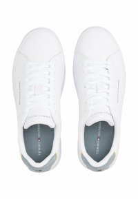 Białe sportowe sneakersy z gładką skórzaną wierzchnią warstwą, zawiązywaniem na sznurówki, wyściełanym kołnierzem i szarym wnętrzem. Żółty akcent przy pięcie.