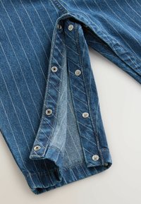 Modra-denim tkanina z navpičnimi belimi črtami, ki ima kapice na notranji šiv. Odsotna tekstura na robovih.