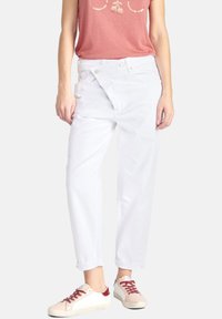 Witte wijde jeans met een relaxte pasvorm, voorzien van een zijknoopsluiting en opgerolde manchetten, gecombineerd met lichtgekleurde sneakers.