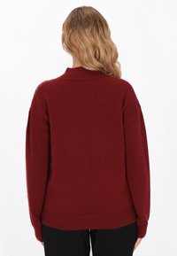 Maglione color bordeaux con colletto a costine e maniche morbide. Texture soffice con una vestibilità leggermente oversize, caratterizzato da sottili dettagli di cucitura.