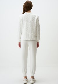 Witte gebreide trui met een geometrisch patroon, gecombineerd met bijpassende taps toelopende broek. Sneakers in een lichte kleur maken de outfit compleet.