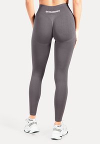 Leggings gris taille haute en tissu extensible, avec des détails de contour subtils et un logo blanc sur la ceinture.