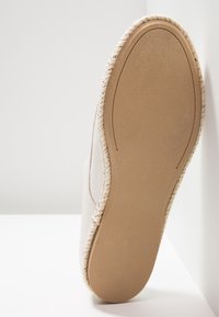 Espadrille avec tige en textile beige clair, bordure en jute tissée, et semelle en caoutchouc beige avec un design lisse et arrondi.