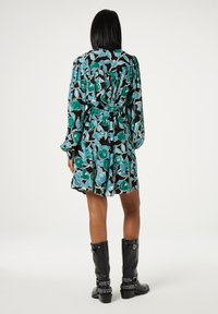 Blumenkleid mit schwarzem Hintergrund, das blau- und grüne Muster aufweist, lange Ärmel, tailliert und mit plissiertem Rock. Getragen mit schwarzen Stiefeln bis zum Knie.