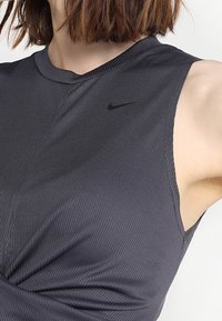 Ciemnoszary sportowy top bez rękawów z prążkowaną fakturą i zaokrąglonym dekoltem. Na klatce piersiowej dyskretne czarne logo Nike.
