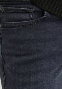 Mörka denimjeans med en slät textur, med en framficka och kontrasterande sömmar. Tyget har subtila blekningar och tonade detaljer.