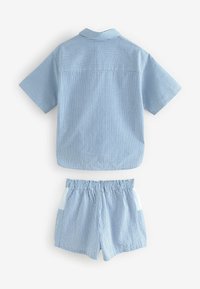 Prugasta plava košulja kratkih rukava s ovratnikom i odgovarajuće kratke hlače s elastičnim strukom i dva bočna džepa. Mekani, lagani materijal.