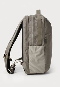 Gray fabric backpack with a side pocket, two zippers, and adjustable straps. Front panel features a smooth texture and reinforced stitching.