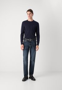 Marineblaues Langarmshirt mit kleinem Logo, kombiniert mit dunkelblauer Jeans und schwarzen Schuhen. Einfaches Design mit klassischer Passform.