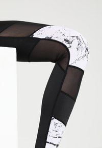 Leggings da allenamento in bianco e nero caratterizzati da un motivo marmorizzato, pannelli in rete e tessuto testurizzato, con un design aderente e cuciture a contrasto.