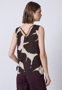 Haut sans manches présentant un motif floral brun foncé et crème, avec un décolleté en V et des bretelles croisées dans un tissu léger.