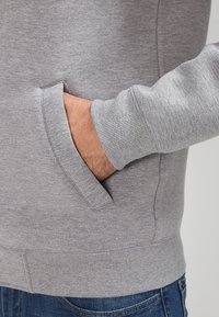 Gray sweatshirt with a textured finish, featuring a side pocket and ribbed cuffs. Visible stitching detail along the seams.